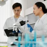 Asian scientists in lab coats discussing research with a microscope in a laboratory setting.