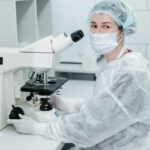 A female scientist in protective gear using a microscope in a lab setting.