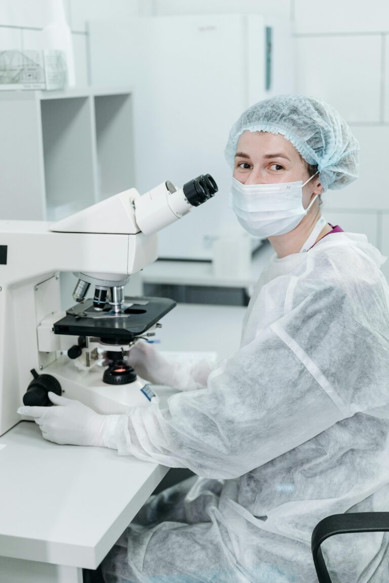 A female scientist in protective gear using a microscope in a lab setting.